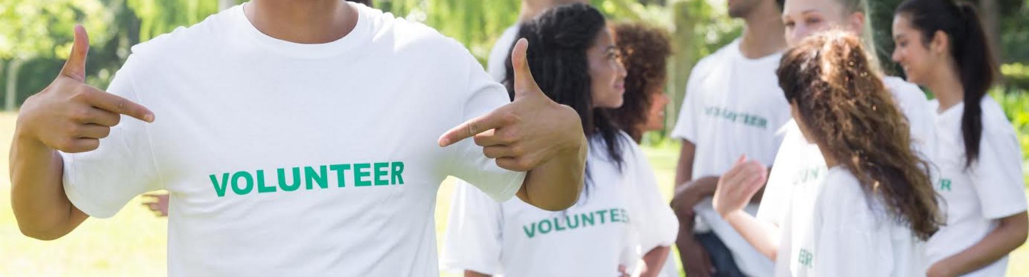image of young man with Volunteer Tshirt on as he points to the word volunteer on his Tshirt